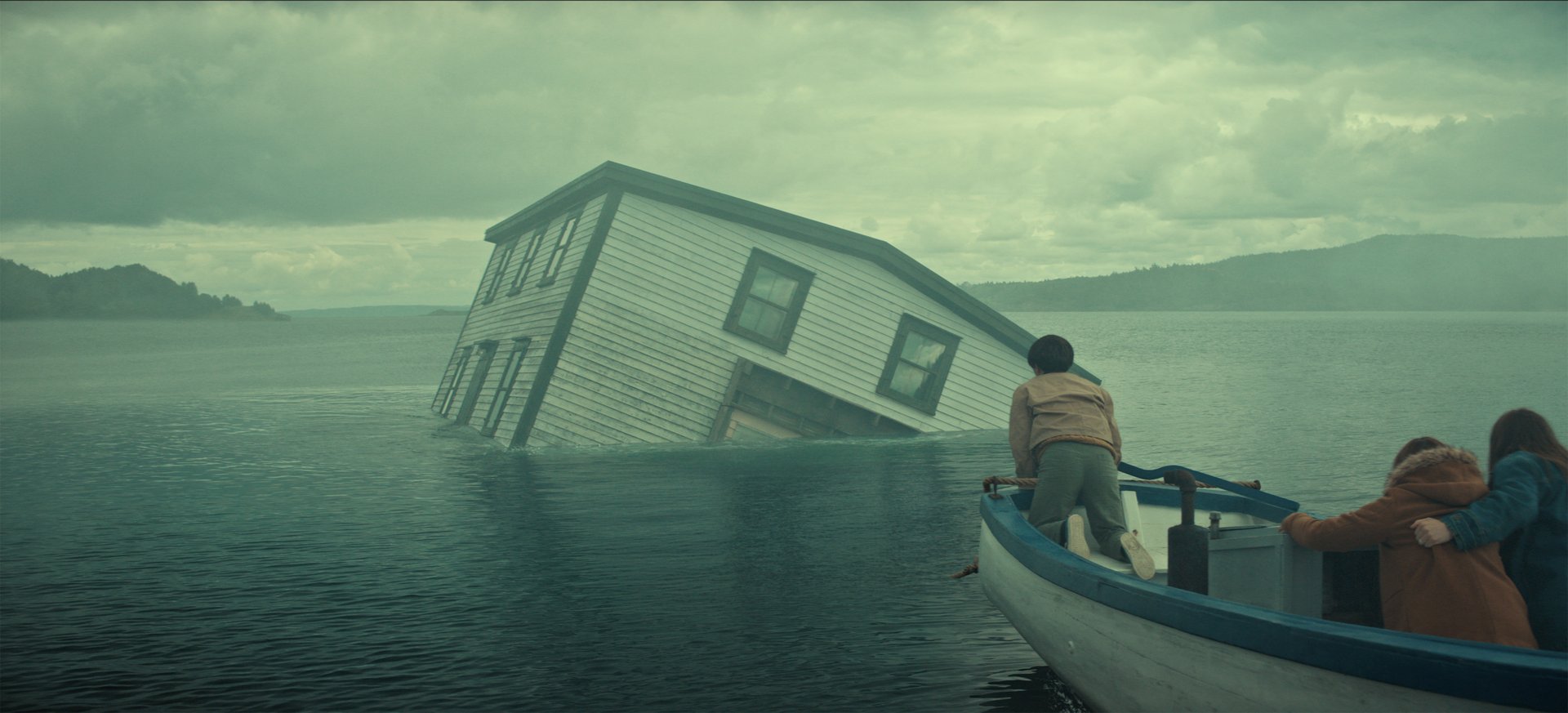 "A partially submerged house tilts in a misty lake as three people in a small boat observe, with cloudy skies and distant hills creating a dramatic, mysterious atmosphere."